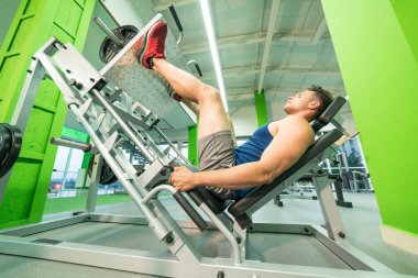 Spor merkezinde bacak egzersizi yapan adam.