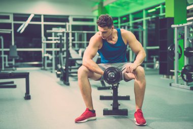 Sporcu spor salonunda bir dambılla egzersiz yapıyor.