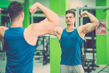 Sporcu, spor salonunda aynanın önünde poz verir.