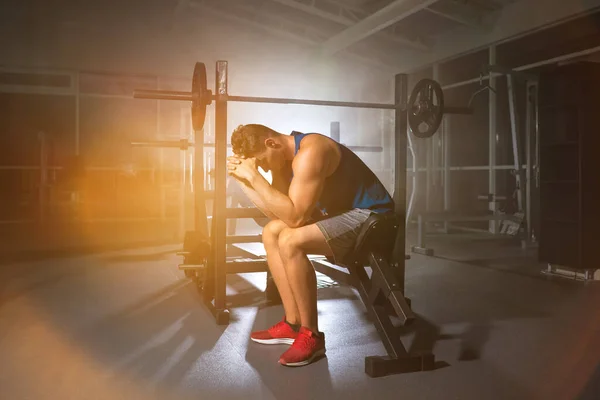 The man sit on a bench in the gym on the bright light background