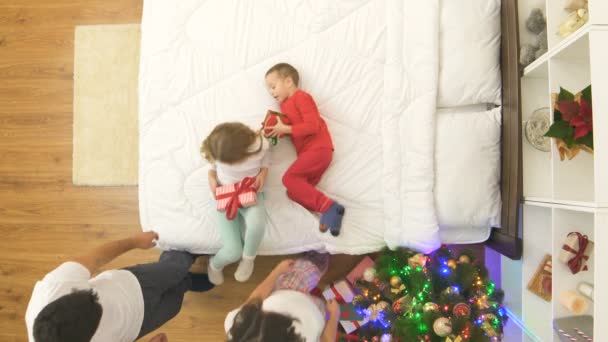 Ευτυχισμένη Οικογένεια Ξεπακετάρει Δώρα Στο Κρεβάτι Κοντά Ένα Χριστουγεννιάτικο Δέντρο — Αρχείο Βίντεο