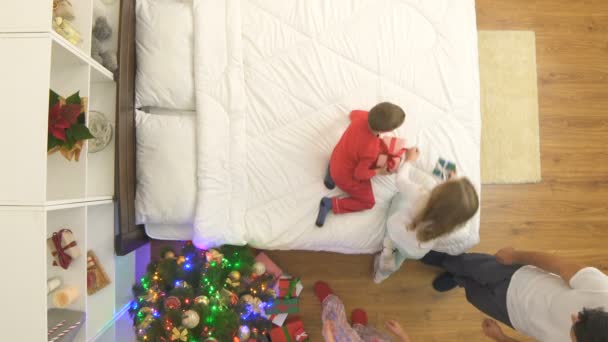 家族はクリスマスツリーの近くのベッドで贈り物をアンパックします 上からの眺め — ストック動画