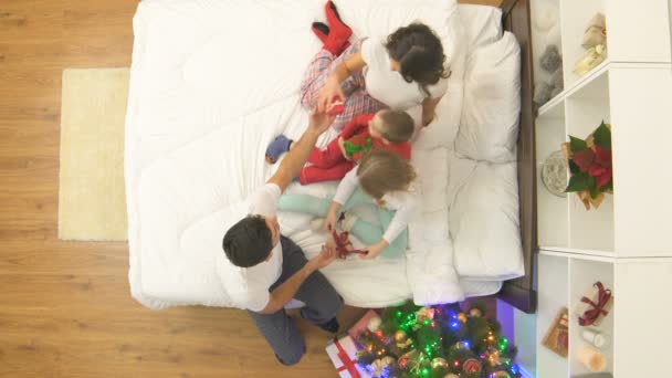幸せな家族はクリスマスツリーの近くの贈り物とベッドの上に座っています 上からの眺め — ストック動画