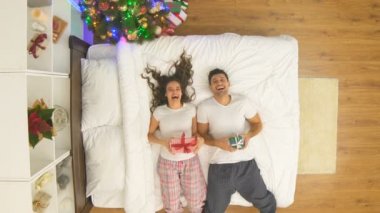 Hediyeli mutlu çift Noel ağacının yakınındaki bir yatağa atlıyor. Yukarıdan görünüm