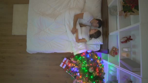 这对幸福的夫妇在靠近圣诞树的床上拥抱 傍晚时分 — 图库视频影像