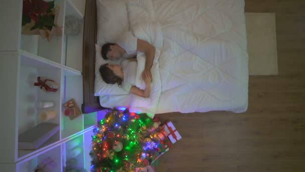 这对幸福的夫妇在靠近圣诞树的床上拥抱 从上往下看 — 图库视频影像