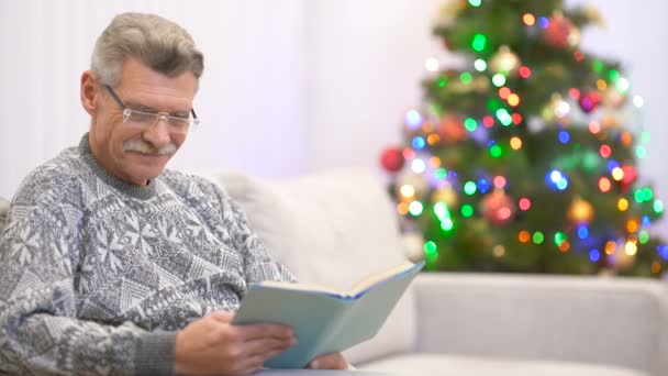 Pensionato Legge Libro Sorride Vicino All Albero Natale — Video Stock