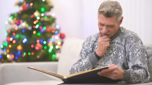 那位快乐的退休老人在圣诞树旁看书 微笑着 — 图库视频影像