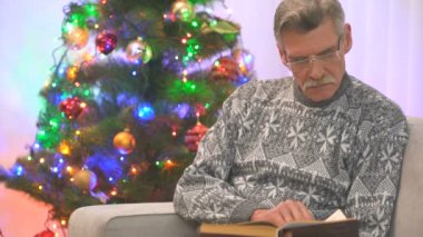 Mutlu yaşlı adam Noel ağacının yanında bir kitap okudu. Akşam vakti.