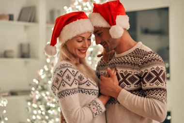 Mutlu adam ve kadın yılbaşı ağacının arka planında duruyorlar.