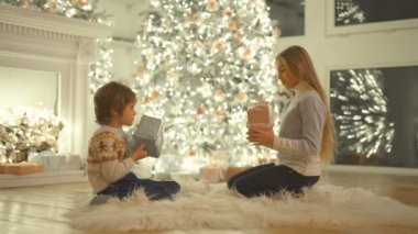 Mutlu çocuk ve bir kız Noel ağacının yanında oturuyor ve hediye kutusunu sallıyorlar.