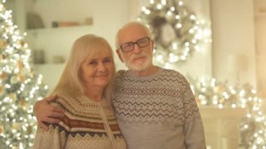 Mutlu yaşlı kadın ve adam, Noel ağacının arka planında sarılıyor.