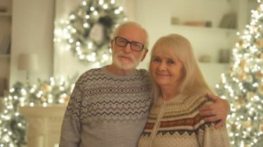 Mutlu yaşlı kadın ve adam Noel ağacının yanında sarılıyor.