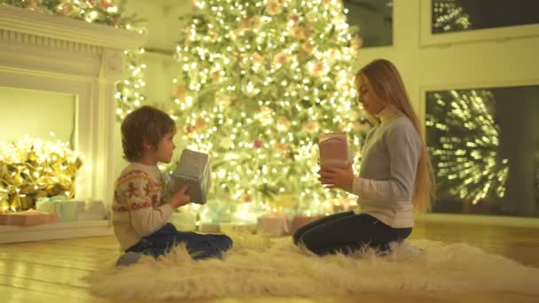 Jongen Een Meisje Zitten Naast Kerstboom Schudden Geschenkdozen — Stockvideo