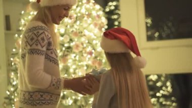 Anne, Noel ağacının yanında kızına hediye veriyor.