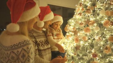 Kırmızı şapkalı aile güzel Noel ağacını süslüyor. yavaş çekim