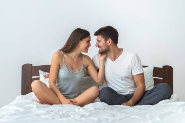Beyaz arka planda, yatakta oturan mutlu adam ve bir kadın.