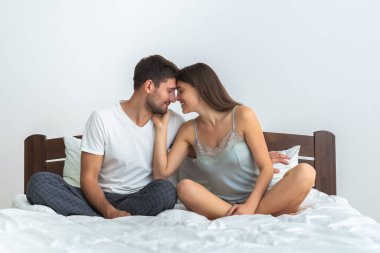 Beyaz arka planda, yatakta oturan mutlu adam ve bir kadın.