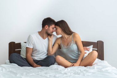 Beyaz arka planda, yatakta oturan mutlu çift.