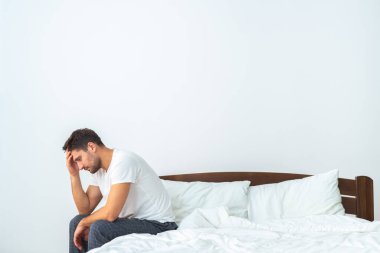 Mutsuz adam beyaz arka planda yatakta oturuyor.