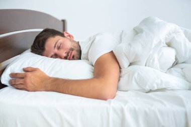 Beyaz arka planda, yatakta uyuyan adam.