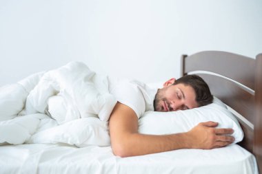 Beyaz arka planda yatakta uyuyan yakışıklı adam.