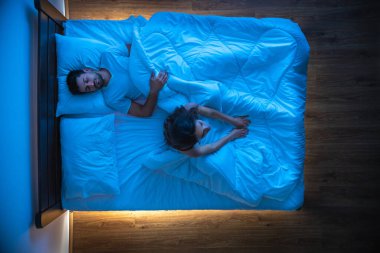 Yatakta uyuyan bir adamın yanında uykusuzluk çeken kadın. Yukarıdan görünüm