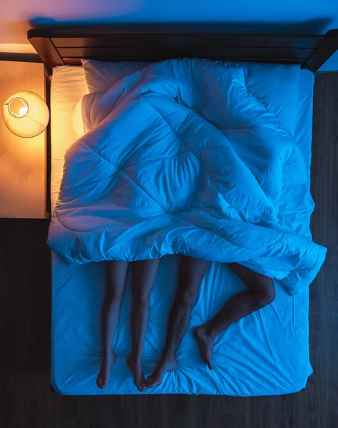 The couple laying under a duvet on the bed. evening night time, view from above