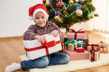 Mutlu çocuk Noel ağacının yanında bir hediye kutusuyla oturuyor. 