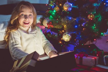 Kız hediyeyi Noel ağacı arka planına yerleştirdi. Akşam vakti.