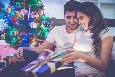 Mutlu adam ve bir kadın yılbaşı ağacının yanındaki hediye kutusunu açıyor.