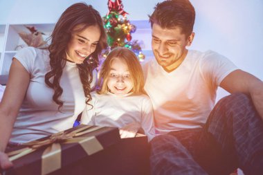 Kızı ve ailesi yılbaşı ağacının yanındaki ışık kutusunu açıyor.
