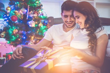 Erkek ve kadın yılbaşı ağacının yanındaki hediye kutusunu açıyor.