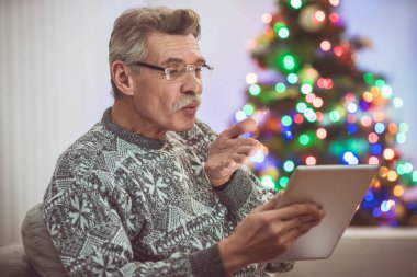 Tabletli emekli, Noel ağacının yanında bir video görüşmesi yapıyor.