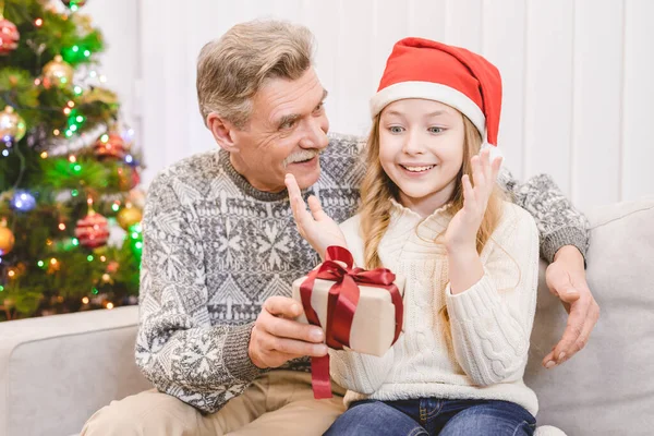 The happy grandfather giving a gift box to a little girl