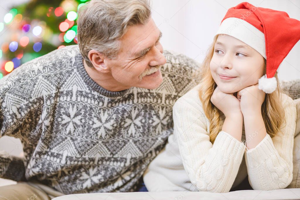 The happy girl in a santa claus hat sit near the grandfather 