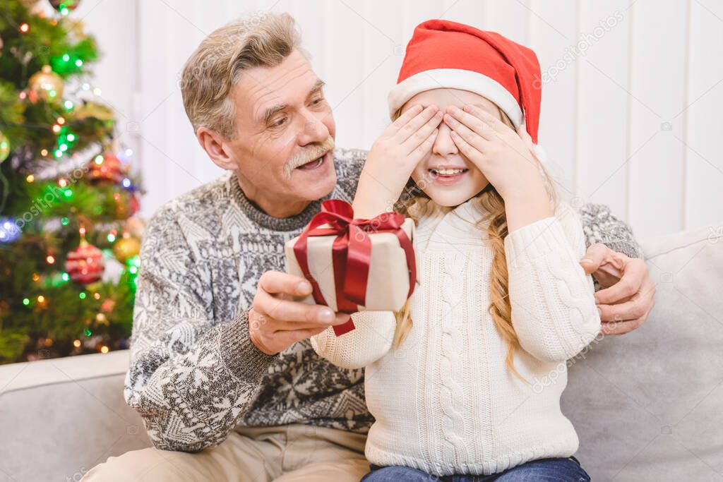 The happy grandfather giving a gift box to a little girl