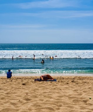 Yaz boyunca plajda uzanan bir adam, Endonezya, Bali 'de arka planda eğlenen insanlarla birlikte. Yazın Bali plajları