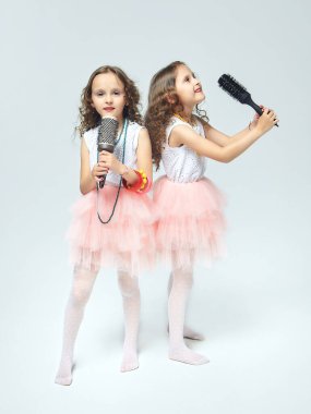 İki küçük kız birbirlerinin saçlarını tarıyor. Saç fırçalarına şarkı söyleyen ikiz kız kardeşler. beyaz sırt