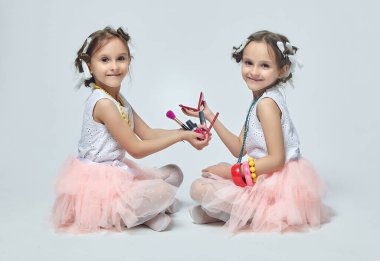 İki küçük kız annelerinin makyajıyla oynuyorlar. Poz verirler ve yetişkin olmaya çalışırlar. Stüdyo, beyaz sırt.