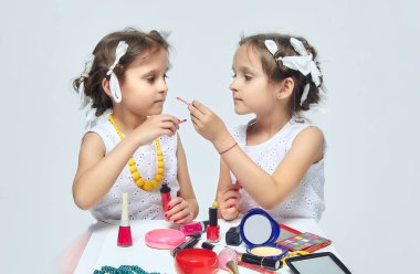 İki küçük kız annelerinin makyajıyla oynuyorlar. Poz verirler ve yetişkin olmaya çalışırlar. Stüdyo, beyaz sırt.