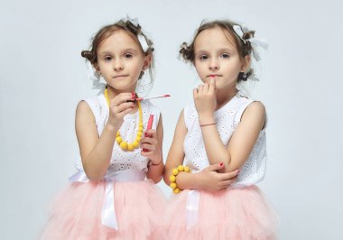 İki küçük kız annelerinin makyajıyla oynuyorlar. Poz verirler ve yetişkin olmaya çalışırlar. Stüdyo, beyaz sırt.