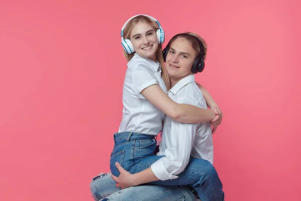 guy and girl in headphones. listen to music while expressing emotions with a kiss. pink back