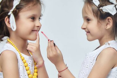 İki küçük kız annelerinin makyajıyla oynuyorlar. Poz verirler ve yetişkin olmaya çalışırlar. Stüdyo, beyaz sırt.