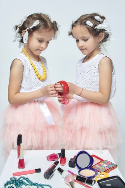 İki küçük kız annelerinin makyajıyla oynuyorlar. Poz verirler ve yetişkin olmaya çalışırlar. Stüdyo, beyaz sırt.