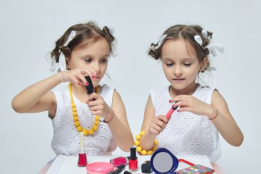 İki küçük kız annelerinin makyajıyla oynuyorlar. Poz verirler ve yetişkin olmaya çalışırlar. Stüdyo, beyaz sırt.