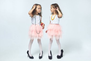 İki küçük kız annelerinin yüksek topuklu ayakkabılarıyla oynuyorlar. Poz verirler ve yetişkin olmaya çalışırlar. Stüdyo, White geri döner.