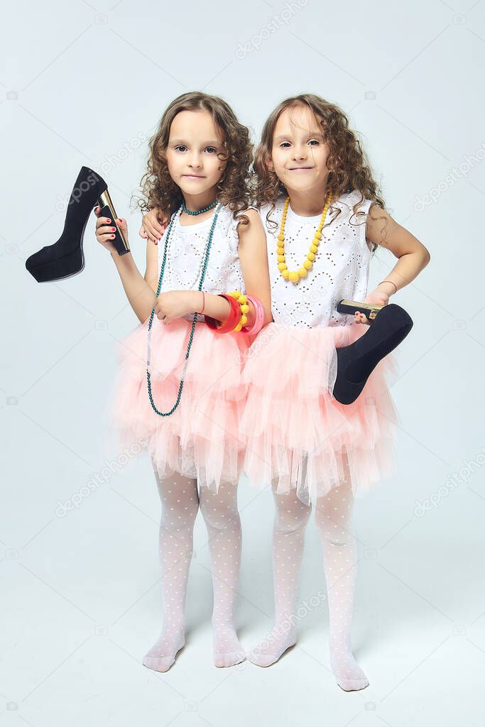 two little girls play with their mother's high-heeled shoes. they pose and try to be adults.Studio, White back