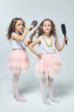 İki küçük kız birbirlerinin saçlarını tarıyor. Saç fırçalarına şarkı söyleyen ikiz kız kardeşler. beyaz sırt