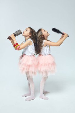 İki küçük kız birbirlerinin saçlarını tarıyor. Saç fırçalarına şarkı söyleyen ikiz kız kardeşler. beyaz sırt